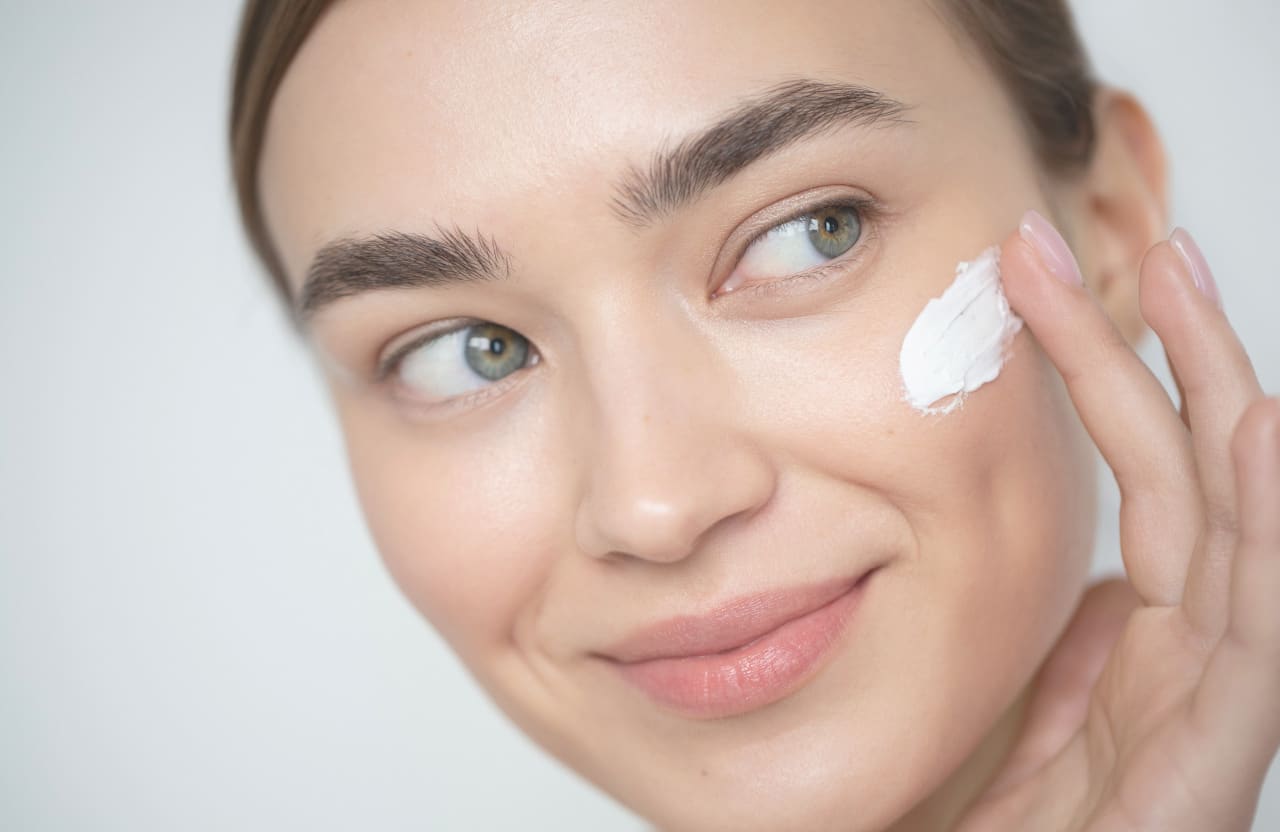 woman smiling while applying a skincare product on her cheek