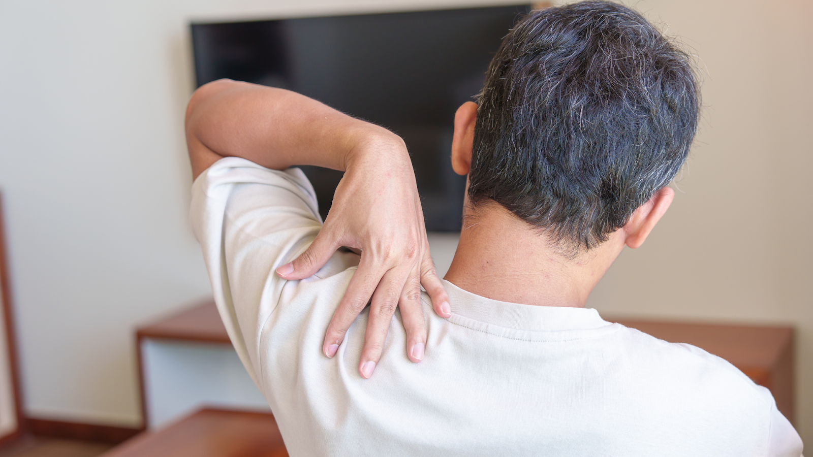 An older individual dealing with pain on their shoulder near the upper back.