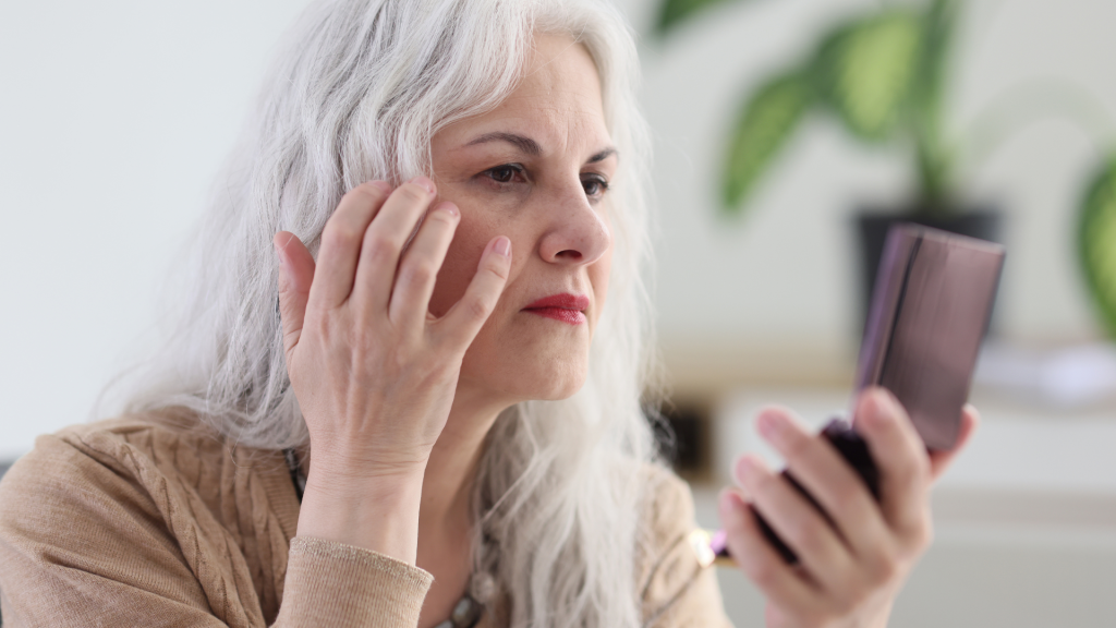 An older woman checking her facial skin condition in a mirror.