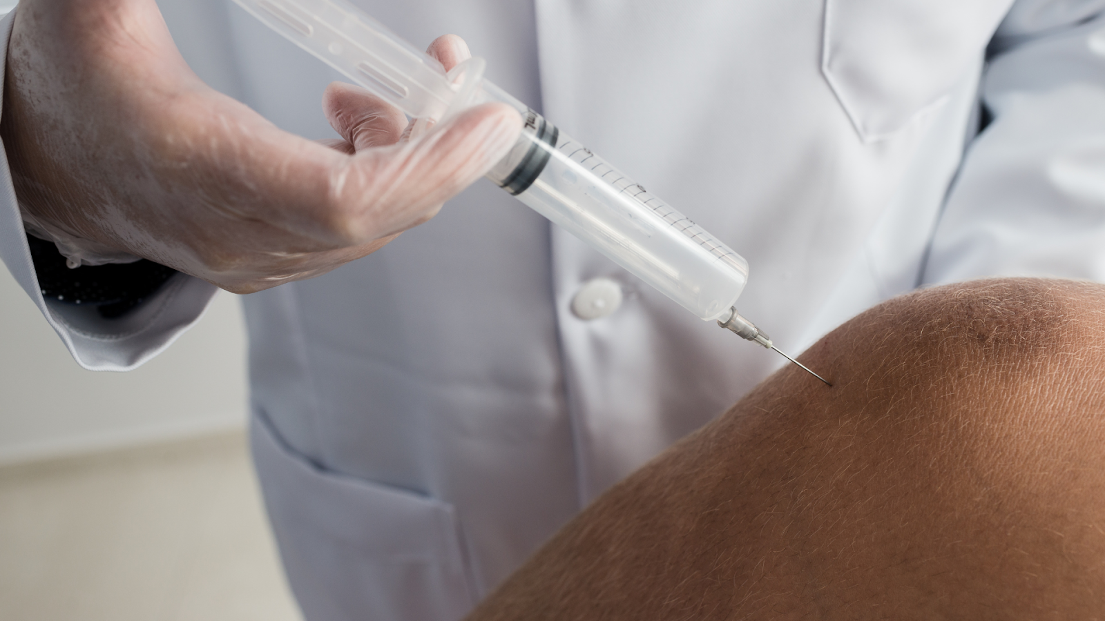 An experienced doctor injecting a syringe into a patient's knee.