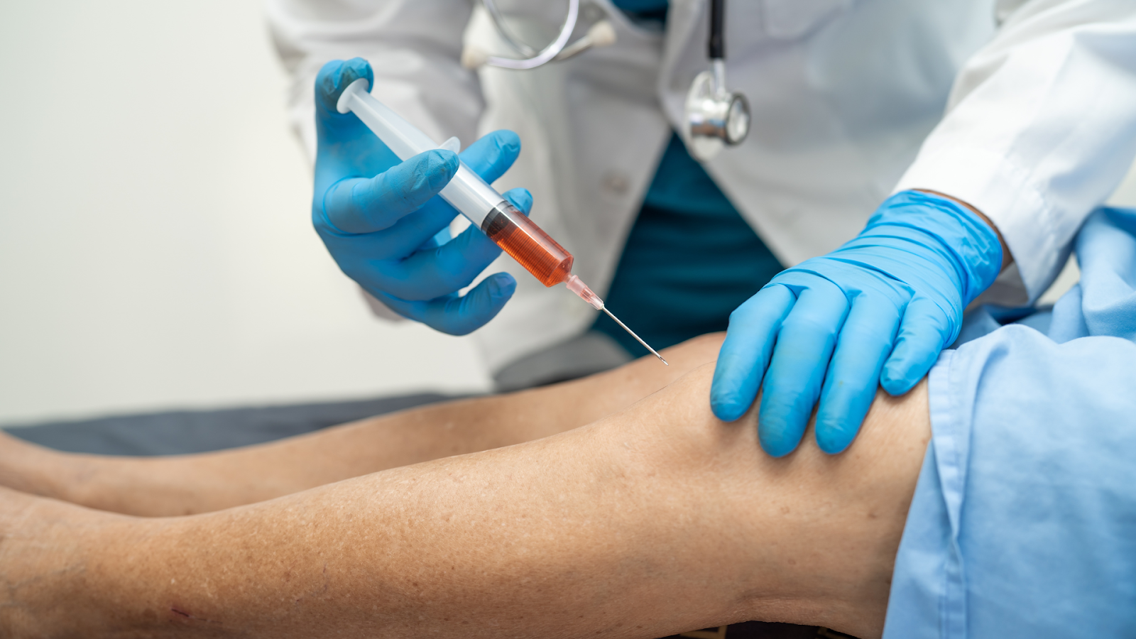 A medical professional injects a treatment into a patient's knee.