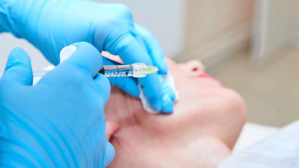 A skilled professional performs a filler injection to the patient's cheek.