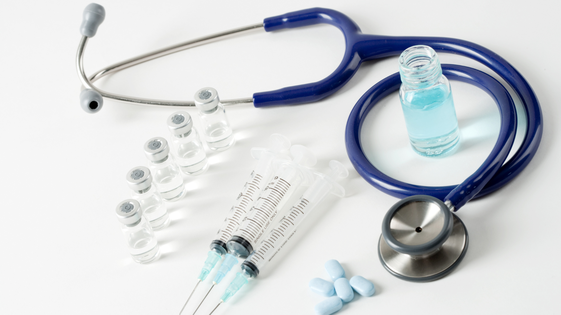 A healthcare provider's stethoscope, medical syringes and vials, and medications.