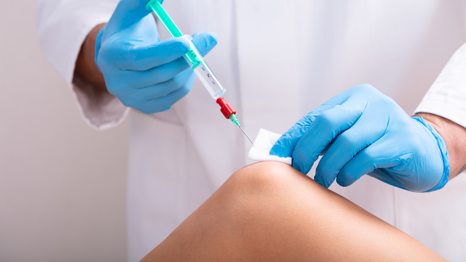 A medical practitioner administering knee injection to a patient.