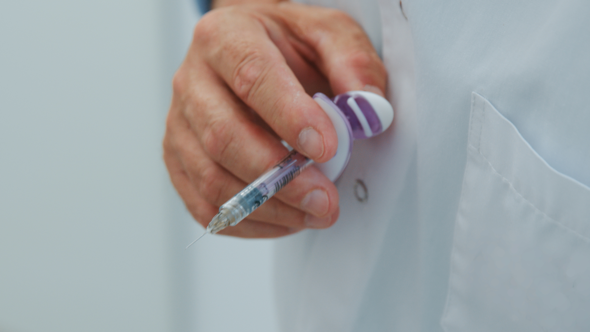 A medical professional holding a syringe for administration.