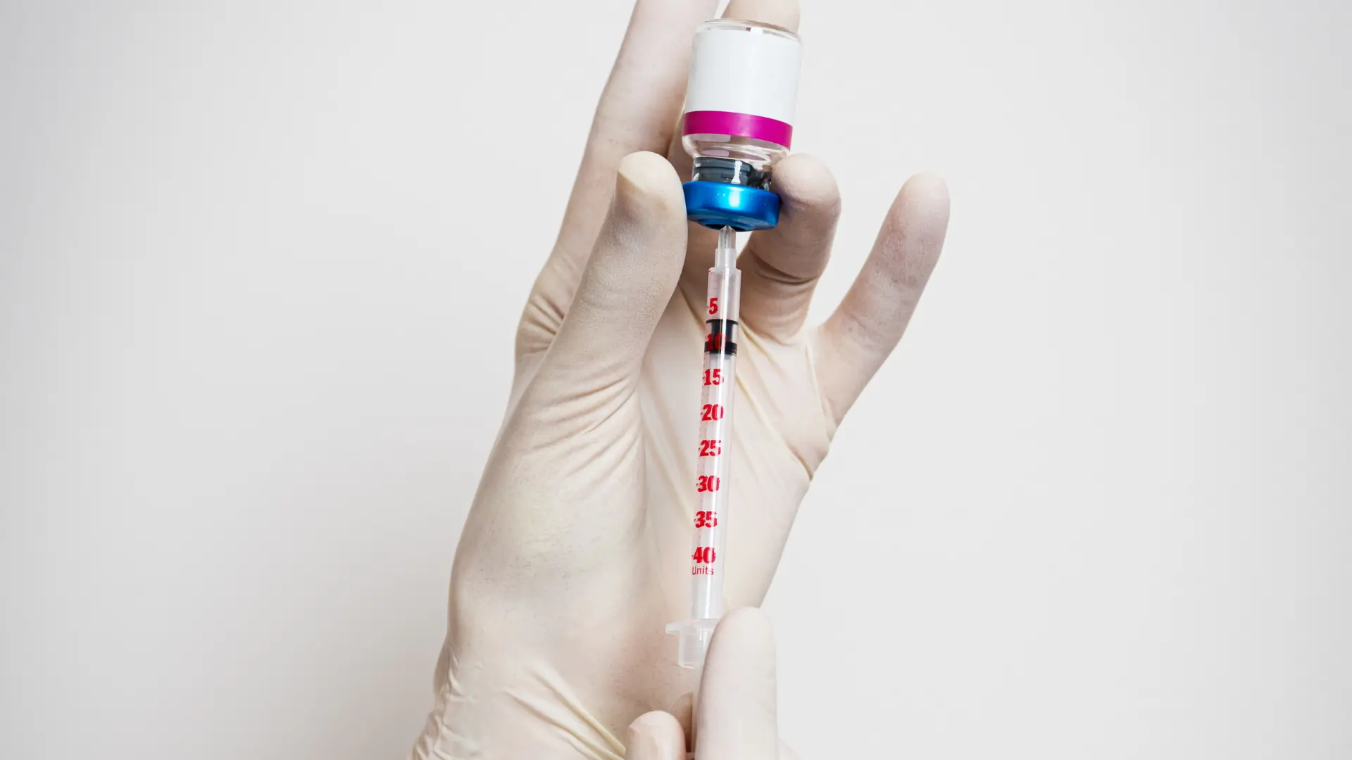 A healthcare provider transferring the contents of a vial to the syringe.