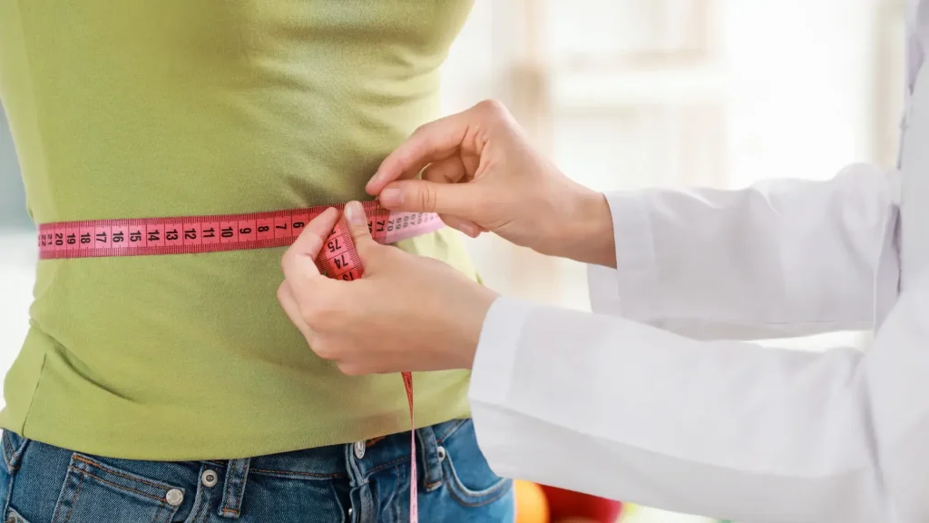 A healthcare provider measuring an individual's waist using a measuring tape.