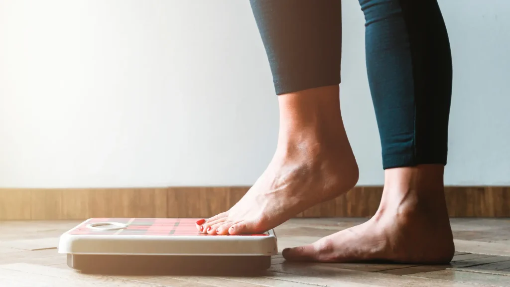 An individual weighing their weight on a scale.