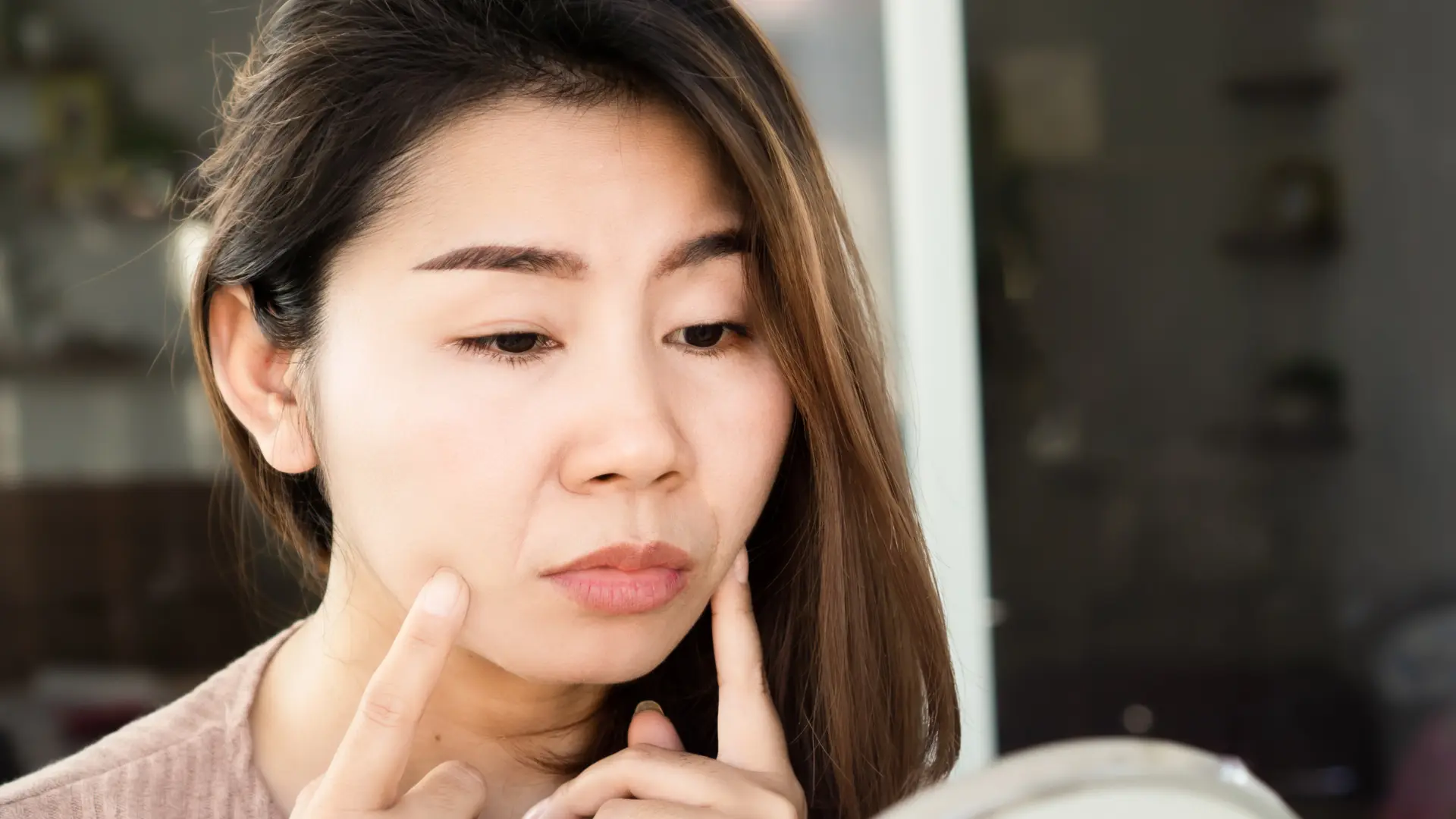 An individual examining their nasolabial folds in the mirror.